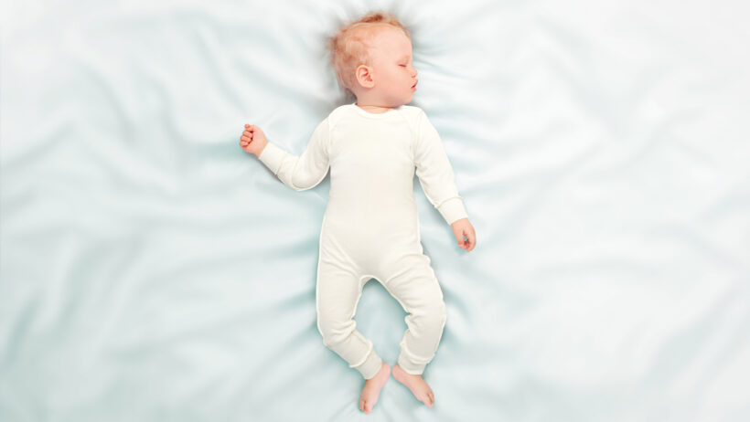 Bébé endormi paisiblement avec un souspyjama blanc pour peau atopique sur drap blanc