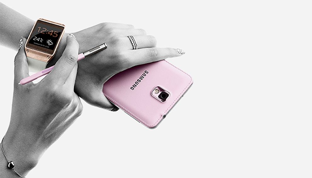 Mains de femme tenant un téléphone Samsung rose et regardant l’heure sur sa montre connectée
