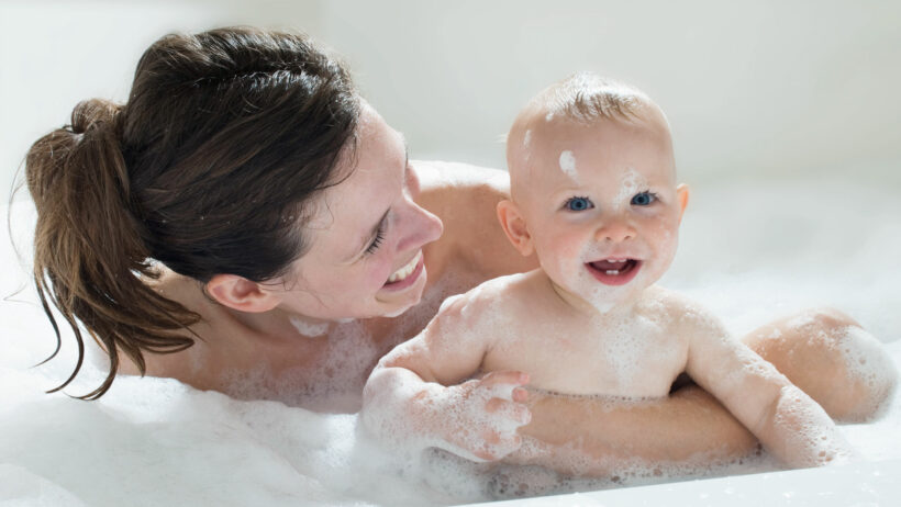 Mère et bébé souriants et jouant dans un bain moussant