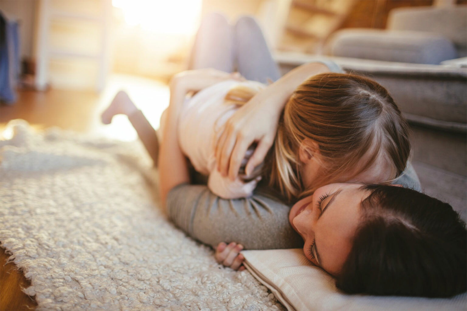 Une mère et sa fille s’enlaçant au sol sur un tapis gris molletonné