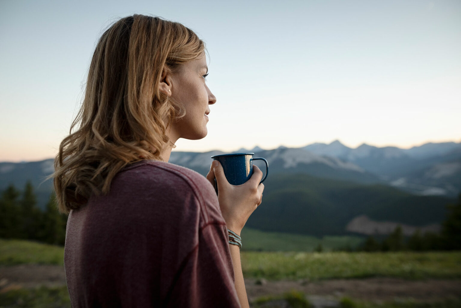 Jeune femme blonde tenant une tasse avec la montagne et des prés en fond