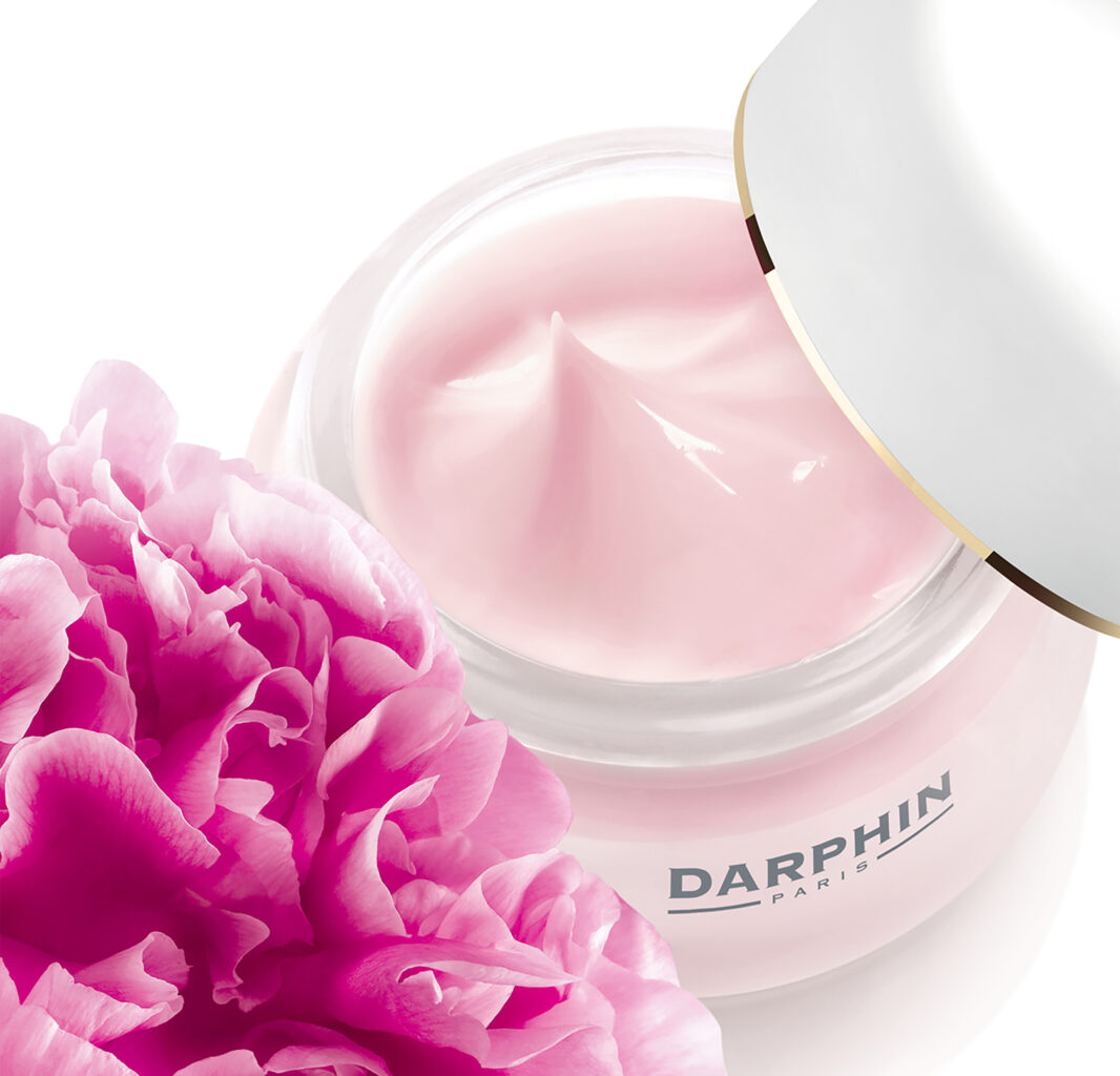 Gros plan sur un pot de crème rose Darphin avec pivoines au premier plan